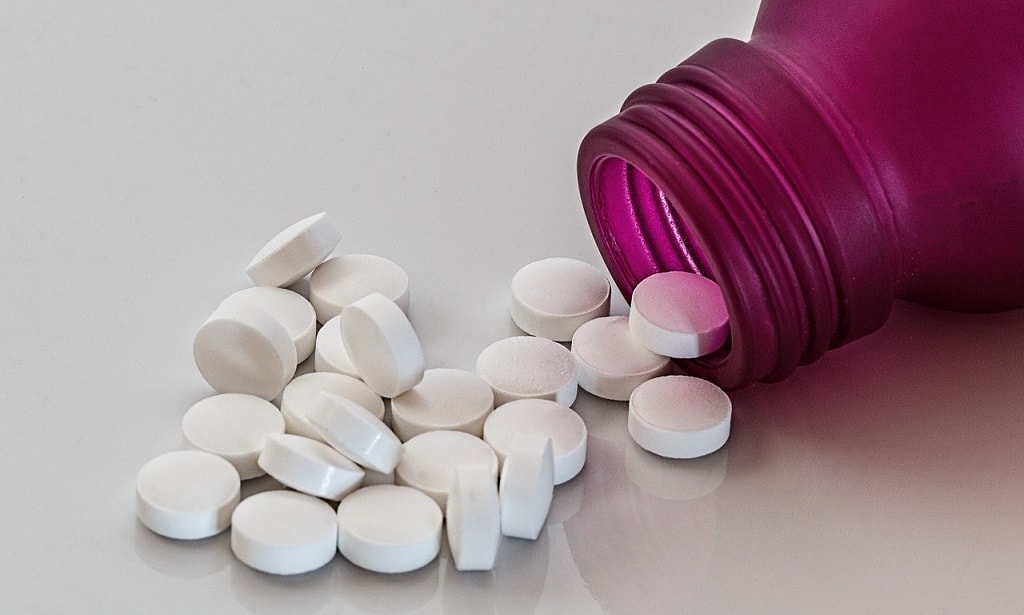 White pills spilling out of pink medication bottle