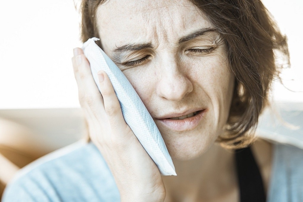 Woman holding ice pack on face for toothache